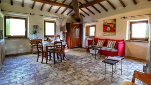 Un coin repas rustique avec une table et des chaises en bois, un canapé rouge et une cuisine en arrière-plan.