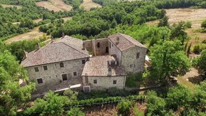 A stone building with multiple rooms and a tower, surrounded by lush greenery and fields. - Belvilla by OYO Regina (Umbertide)