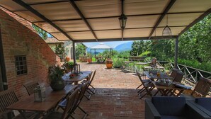 Une terrasse couverte avec un sol en briques, des meubles en bois et une vue sur le paysage environnant.