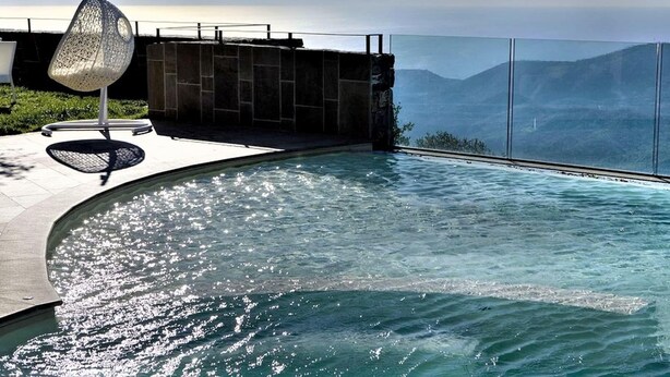 En modern infinitypool med fri utsikt över havet och bergen i bakgrunden.