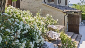 A stone building with a tiled roof, a wooden door, and a small patio area with a table and chairs. - Scenic Villa With Heated Pool (Sant'Ippolito)