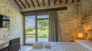 A bedroom with stone walls, a bed with white bedding, a desk, and a TV mounted on the wall. - Scenic Villa With Heated Pool (Sant'Ippolito)