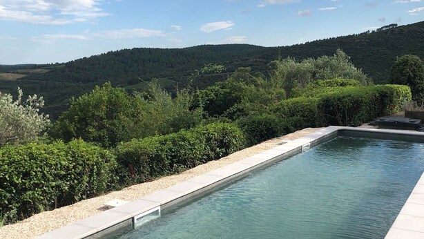 En rektangulär pool med klart vatten, omgiven av en kant av småsten och tät vegetation, med utsikt över en skogbeklädd sluttning.