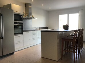 A modern kitchen with a built-in oven, a stainless steel refrigerator, and a large island with bar stools. - Tranquil Vineyard Villa, Berlou (Berlou)