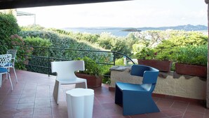 A terrace with two white chairs and a blue chair, a small white table, and potted plants. - Mediterranean Villa of Liscia di Vacca (Arzachena)