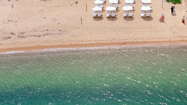 An aerial view of a beach with rows of white beach umbrellas and lounge chairs, a lifebuoy, and a flagpole. - Mediterranean Villa of Liscia di Vacca (Arzachena)