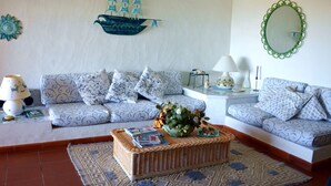 A living room with a sofa set, a decorative ship wall hanging, a mirror, and a wicker coffee table. - Mediterranean Villa of Liscia di Vacca (Arzachena)