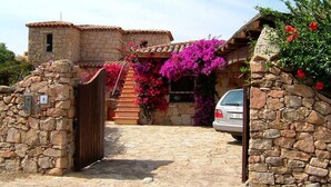 A stone house with a tiled roof, a wooden gate, and a car parked in front. - Mediterranean Villa of Liscia di Vacca (Arzachena)