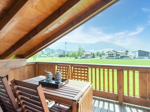 Eine Holzterrasse mit Tisch und Stühlen, die auf ein grünes Feld und Gebäude in der Ferne blickt.