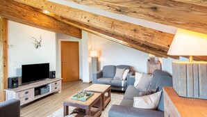 A cozy living room with a wooden ceiling, a flat-screen TV, a grey sofa, and a coffee table.