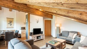A spacious living area with a high wooden ceiling, a television, and seating arrangements including a sofa and chairs.