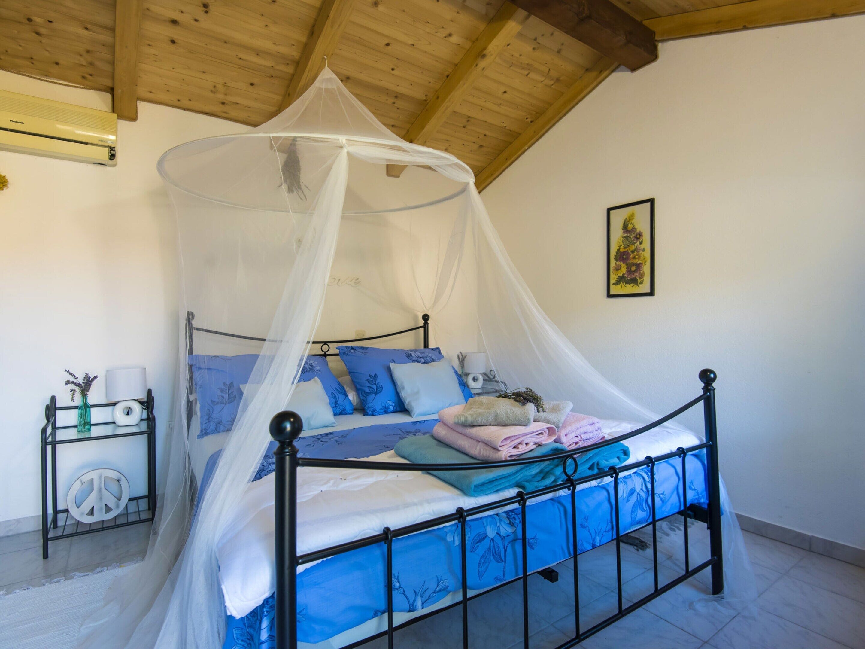 Ein Schlafzimmer mit einem Himmelbett, einem Baldachin, einem Nachttisch mit Lampe und einer Wand-Klimaanlage.