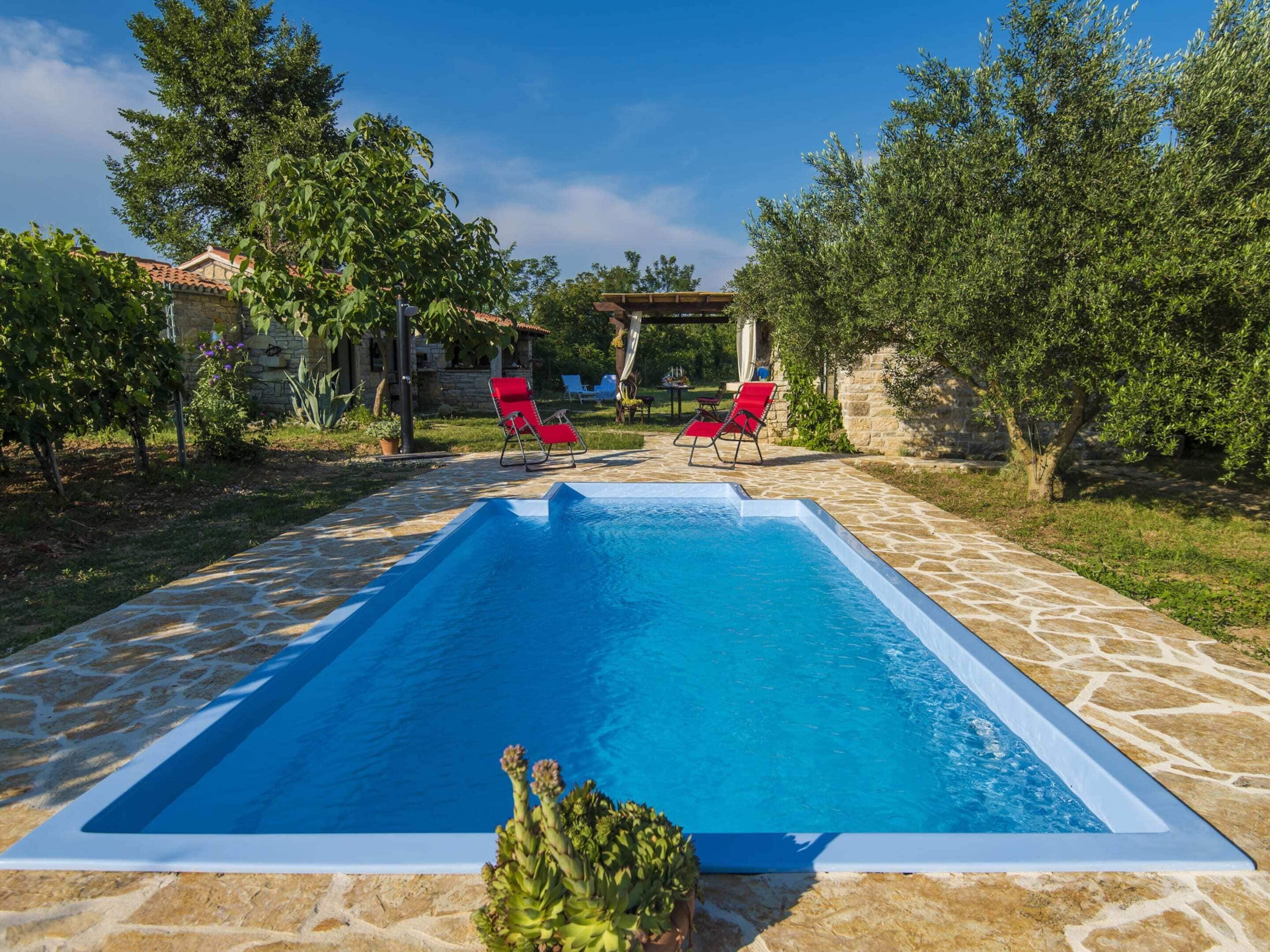 Une piscine rectangulaire revêtue de carrelage en pierre, entourée de verdure et agrémentée de deux chaises longues rouges.