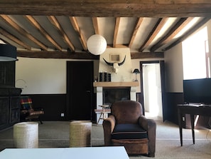 A rustic interior with exposed wooden beams, a fireplace with a bull skull decoration, a leather armchair, and a television. - Holiday Home in Angers With Private Garden (Bierné-les-Villages)