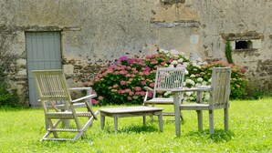 A rustic outdoor seating area with a stone wall backdrop, a wooden bench, and two chairs. - Holiday Home in Angers With Private Garden (Bierné-les-Villages)
