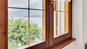 A window with a view of a lake and mountains, a wooden door with a brass handle, and lace curtains.