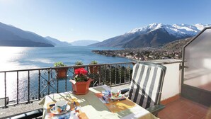 A balcony with a table set for a meal, overlooking a lake and mountains.