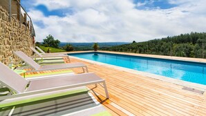 A pool with wooden deck and lounge chairs, surrounded by greenery and a stone wall. - Farmhouse in Vinci With Pool and Tuscan Views (Vinci)