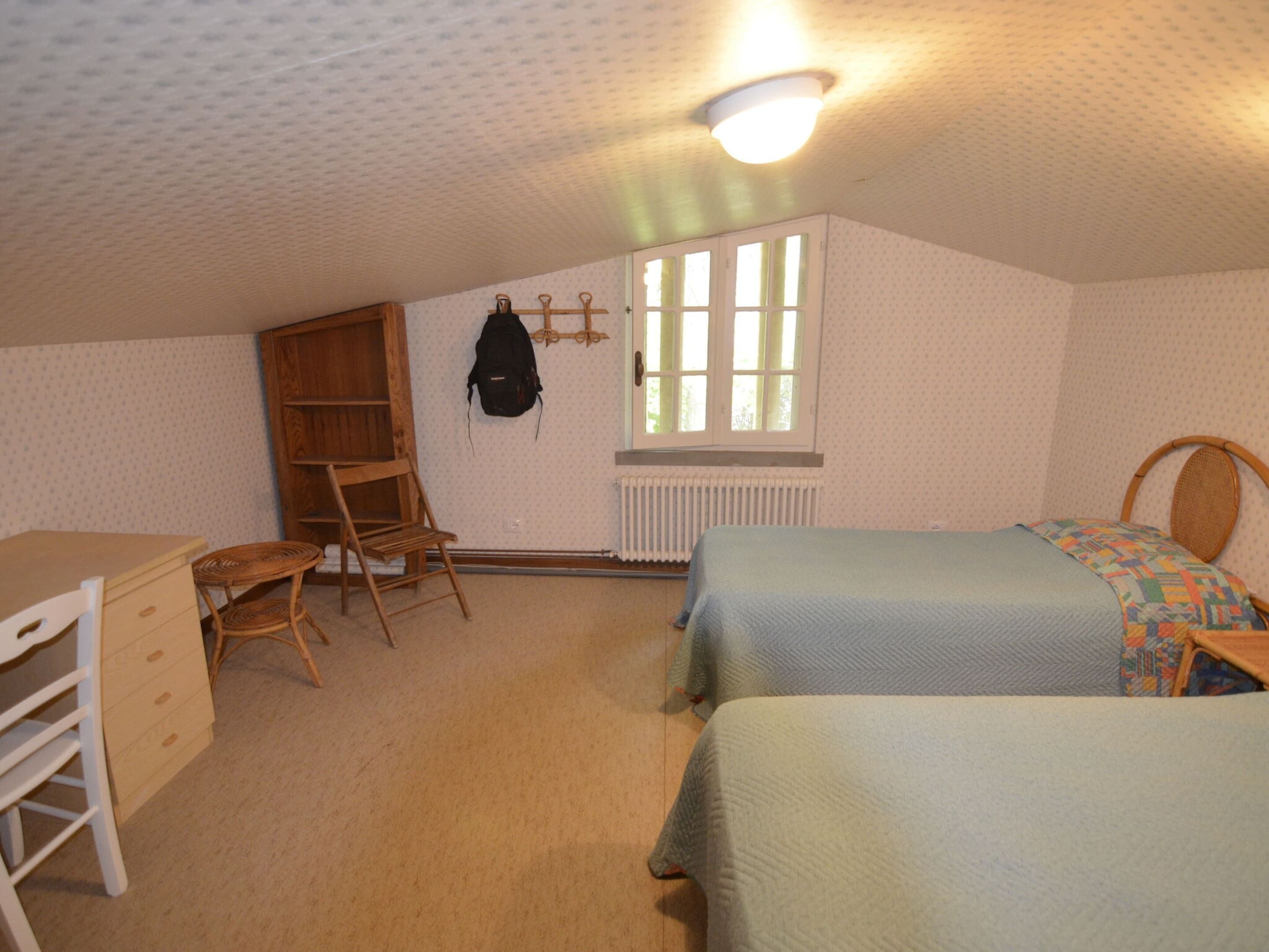 Une chambre avec deux lits, un bureau, une chaise, un radiateur et une fenêtre.
