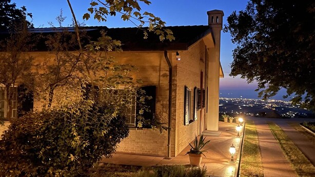 Une maison à deux étages, avec une façade en briques, une cheminée bien visible et un jardin agrémenté de plantes en pot.