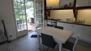Une cuisine moderne avec une table et des chaises blanches, une grande fenêtre et un luminaire suspendu.