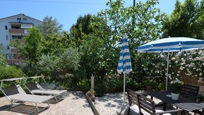 A patio with stone flooring, a table with chairs, and a blue-striped umbrella. - Apartment in Gatteo Mare Near Beach (Gatteo)