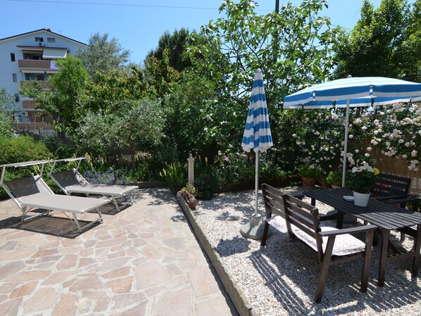 A patio with stone flooring, a table with chairs, and a blue-striped umbrella.