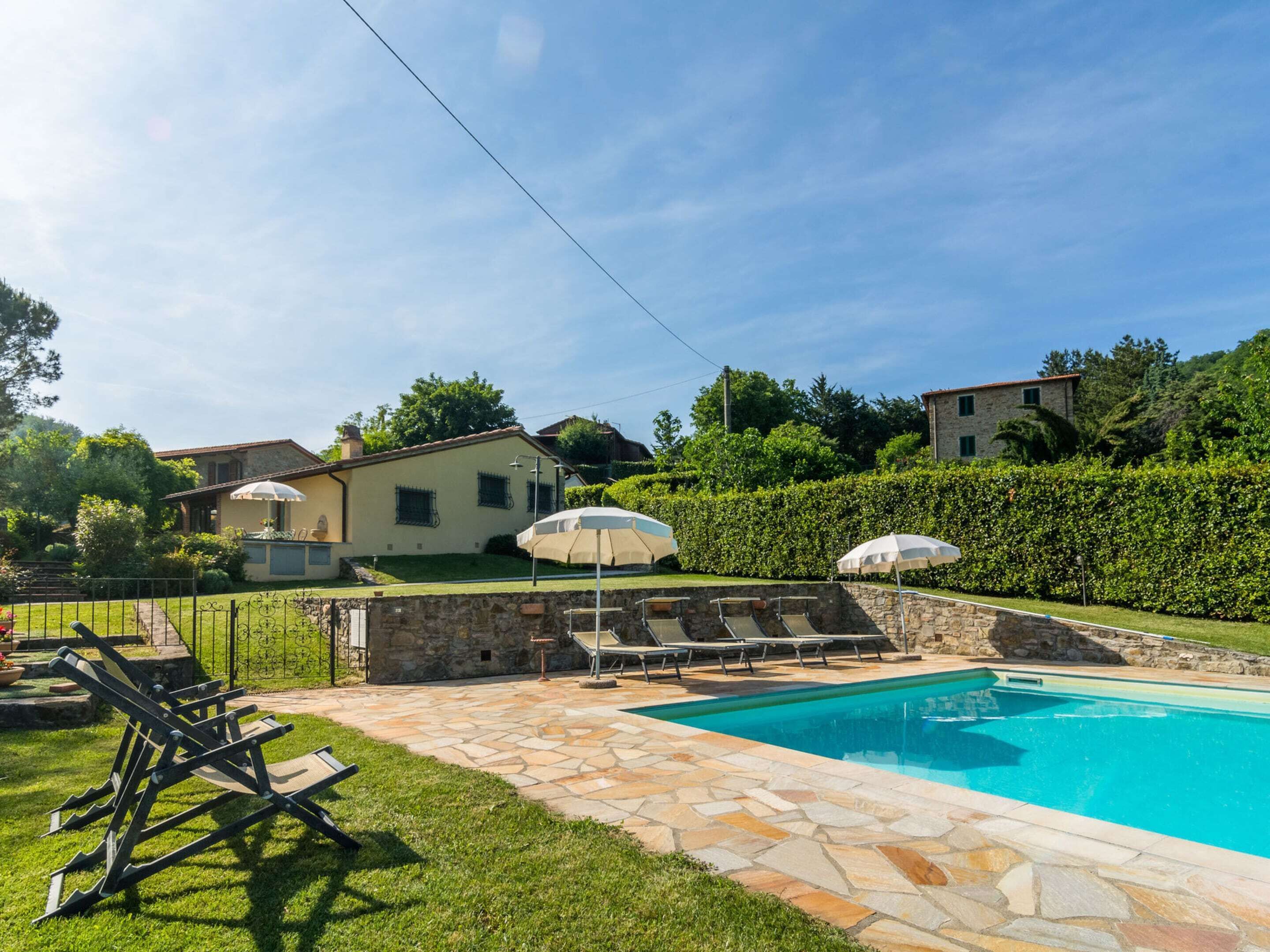 A backyard with a swimming pool, stone patio, and outdoor seating area.