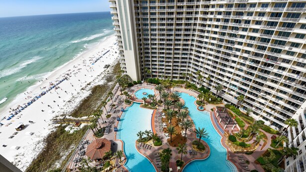 A high-rise hotel with a large pool area, beach access, and multiple balconies.
