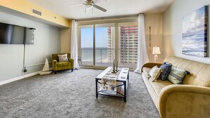 A spacious living room with a large window, a ceiling fan, a flat-screen TV, a sofa, and a coffee table.