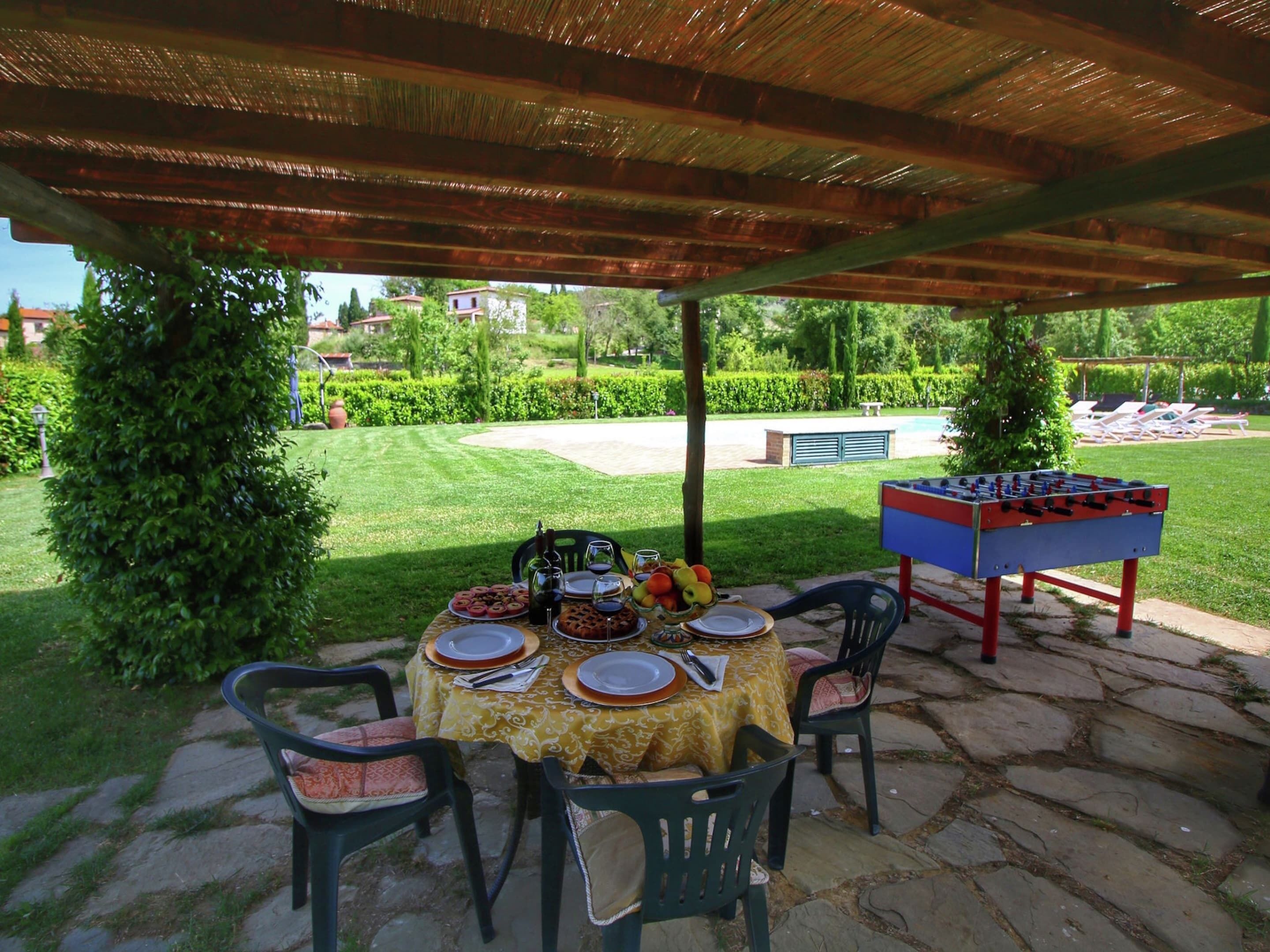 An outdoor patio with a table set for dining, surrounded by chairs, and a foosball table.