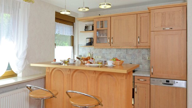 A kitchen with wooden cabinets, a central island with stools, a built-in dishwasher, and pendant lighting.