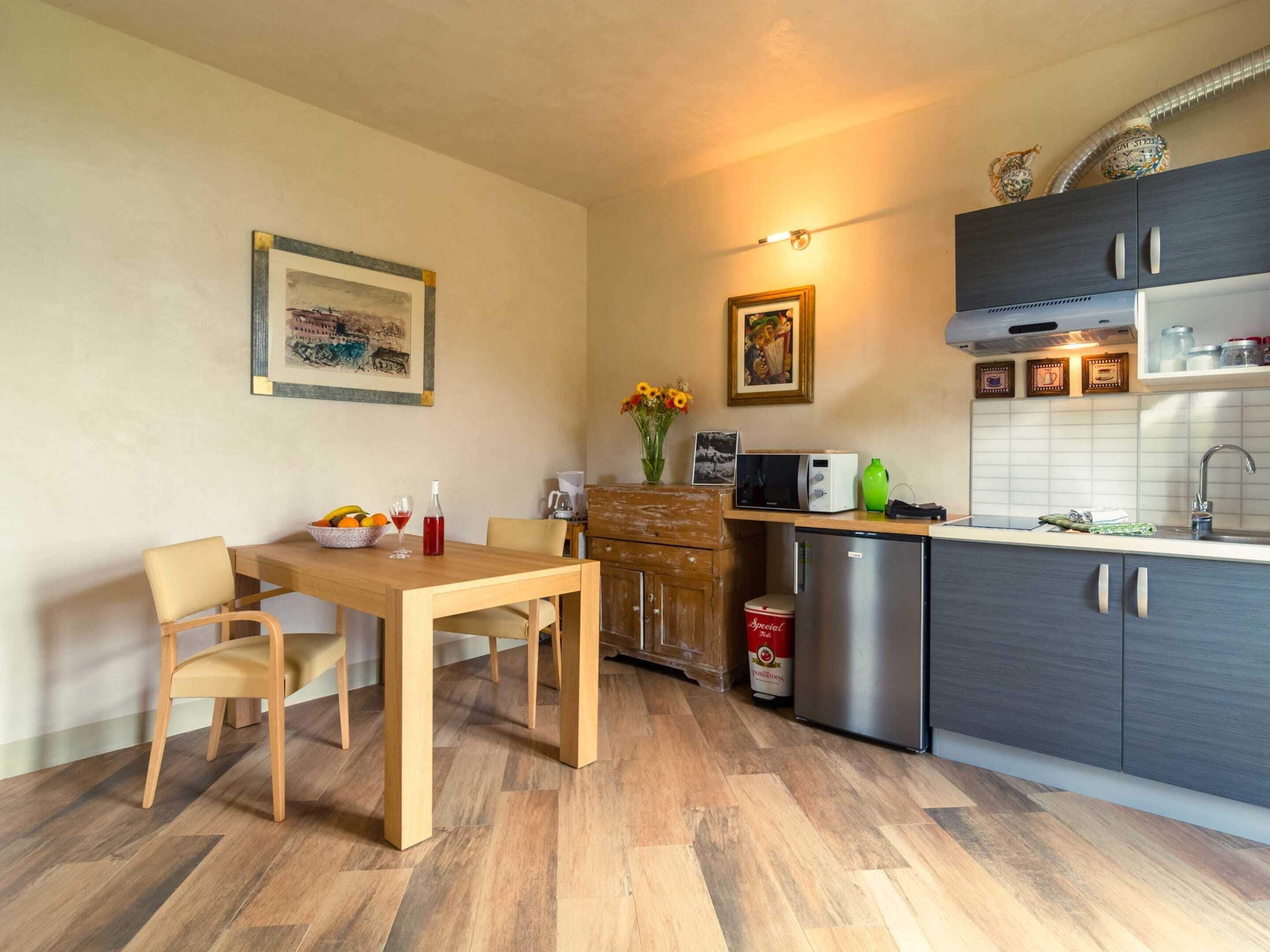 A compact kitchen with a wooden dining table, chairs, a refrigerator, a microwave, and a sink.