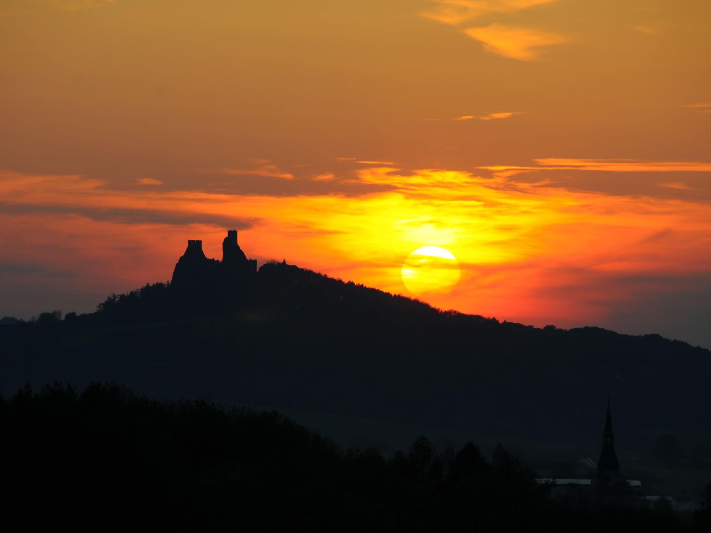 A sunset over a hill with a silhouette of a castle and a church.