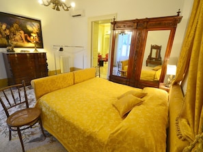 A bedroom with a large bed, a wooden dresser, a chair, and a painting on the wall. - Belvilla by OYO Palazzo Pio (Lecce)