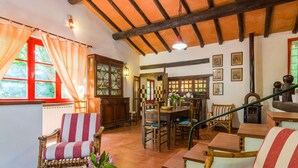 A cozy room with a wooden ceiling, a dining area with chairs, a table with a pitcher and flowers, and a window with curtains. - Belvilla by OYO Due Camini (San Marcello Piteglio)