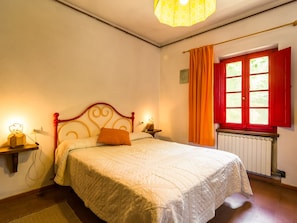 Een slaapkamer met een bed, een nachtkastje, een lamp, een raam met gordijnen en een radiator.