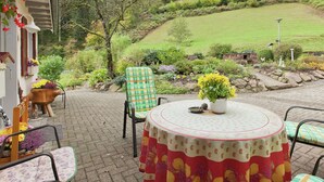 An outdoor patio with a round table and chairs, surrounded by potted plants and a view of a hillside. - Comfy Apartment in Oppenau near Black Forest National Park (Oppenau)
