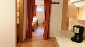 A hallway with wooden flooring, a bed with a window, and a kitchen area with a coffee maker. - Comfy Apartment in Oppenau near Black Forest National Park (Oppenau)