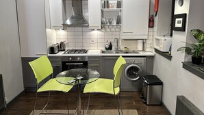 Une cuisine compacte avec des meubles blancs, une cuisinière à gaz, un four à micro-ondes et un lave-linge. On y trouve une petite table à manger avec deux chaises.