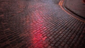 Une rue pavée bordée de bâtiments aux couleurs vives, d’une église et de voitures garées.