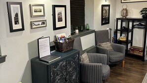 Un salon doté d’un parquet en bois foncé, d’un canapé à rayures, d’un fauteuil vert et d’une console noire ornée de cadres contenant des photos.