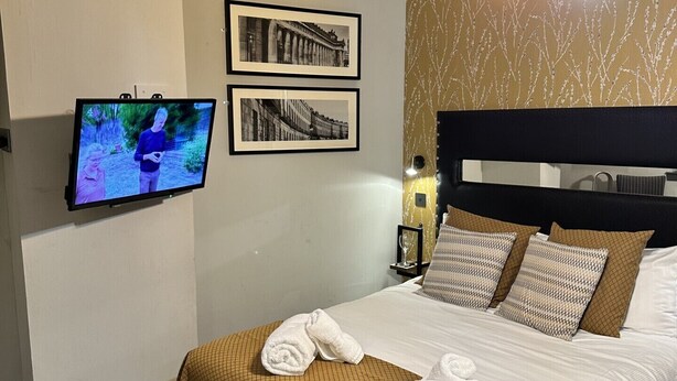 Une chambre d’hôtel avec un lit, un téléviseur fixé au mur et deux tableaux encadrés.