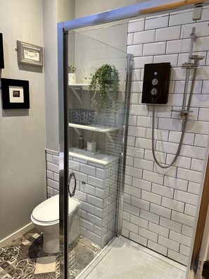 Ein modernes Badezimmer mit Duschkabine aus Glas, Toilette und Waschbeckenbereich mit dekorativen Fliesen und einer Pflanze.