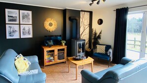 Un salon avec deux canapés bleus, un meuble en bois, une télévision, une cheminée et une grande fenêtre avec des rideaux.