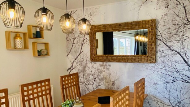 Un espace repas comprenant une table en bois, des chaises, des lampes suspendues et un miroir fixé au mur.