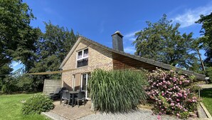 Une maison en briques avec une cheminée, une terrasse avec une table et des chaises, et un jardin avec différentes plantes.