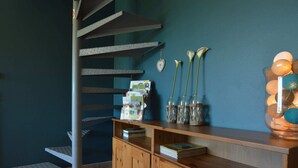 Un escalier en colimaçon avec une finition métallique, une bibliothèque en bois et des objets décoratifs sur un mur de couleur turquoise.
