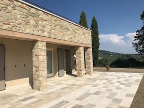 A stone building with a tiled courtyard, large windows, and a view of the countryside. - Tuscan Farm Home Retreat (Chianni)
