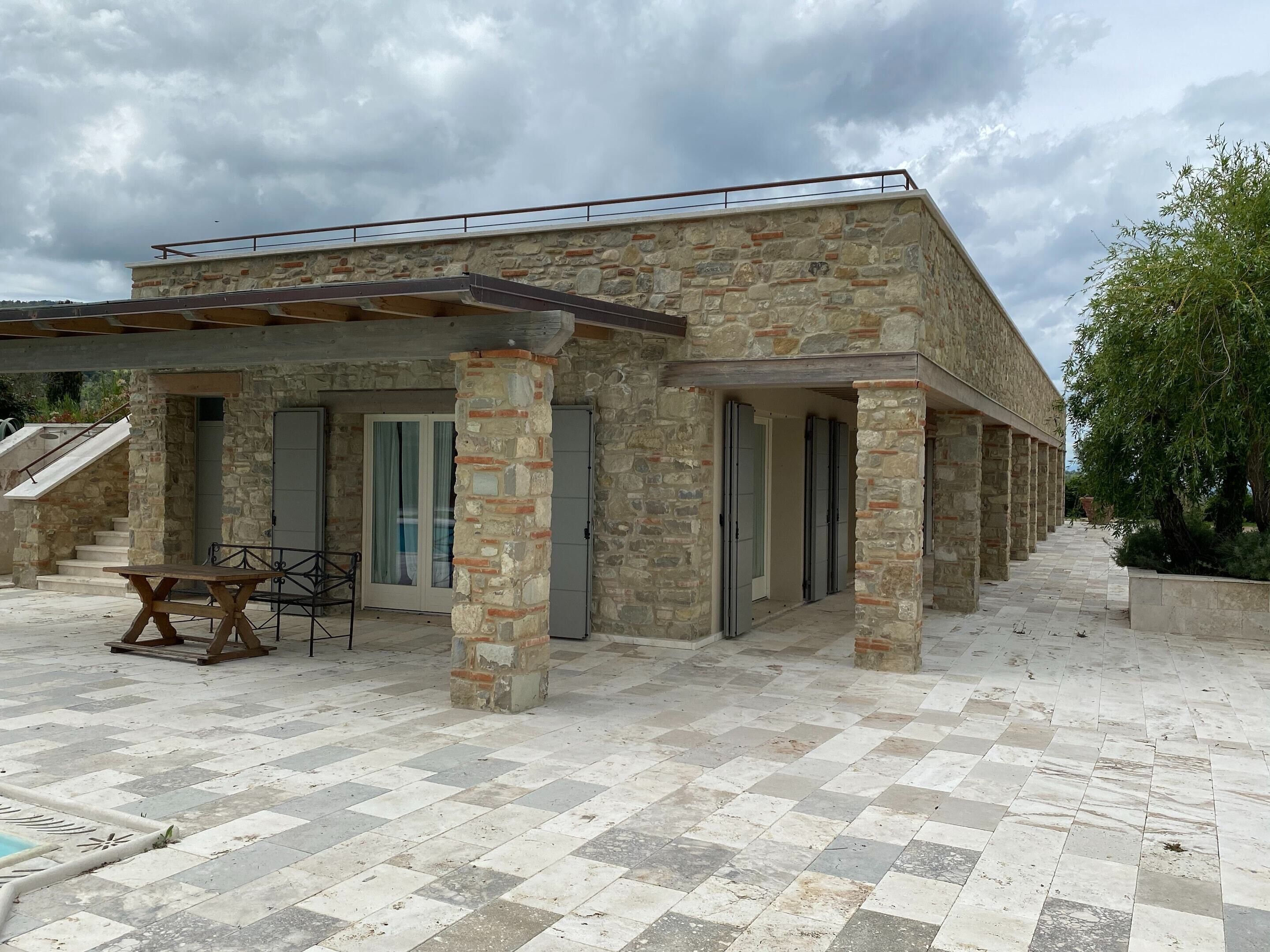 A stone building with a covered patio area, a staircase, and a view of the surrounding landscape.